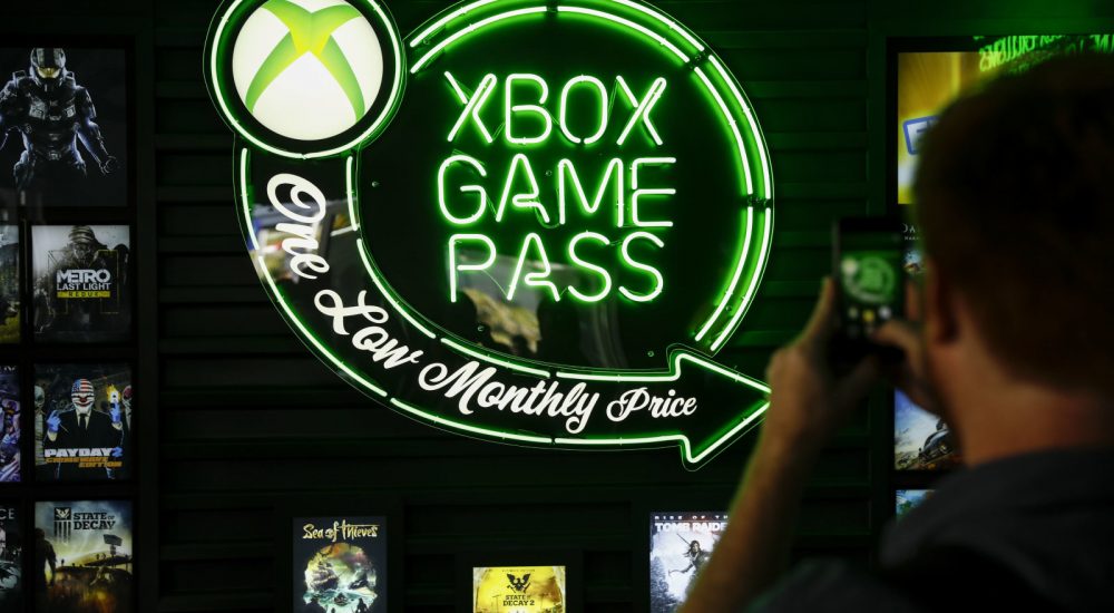 An attendee takes a photograph of Xbox Game Pass signage following the Microsoft Corp. Xbox event ahead of the E3 Electronic Entertainment Expo in Los Angeles, California, U.S., in Los Angeles, California, U.S., on Sunday, June 10, 2018. Xbox previewed a flurry of new titles and deals with studios as the video-gaming division of Microsoft looks to compete more intensely with Sony Corp.'s PlayStation and a resurgent Nintendo Co. Photographer: Patrick T. Fallon/Bloomberg via Getty Images
