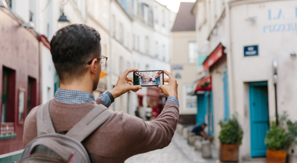 Rear view of a young man taking pictures of Montmartre street with smart phone, Paris, France