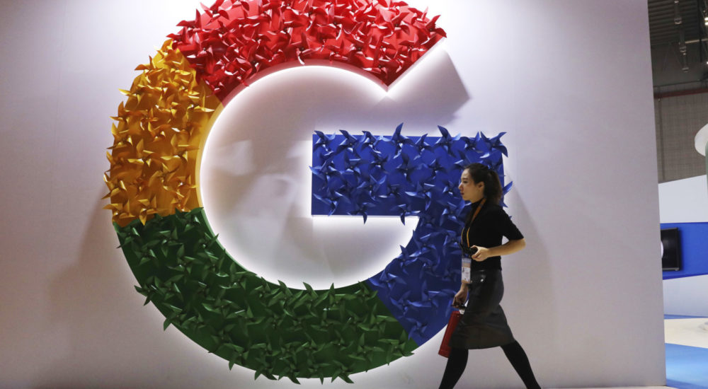 In this Monday, Nov. 5, 2018, photo, a woman carries a fire extinguisher past the logo for Google at the China International Import Expo in Shanghai. Internet traffic hijacking disrupted several Google services Monday, Nov. 12, 2018, including search and cloud-hosting services. (AP Photo/Ng Han Guan)